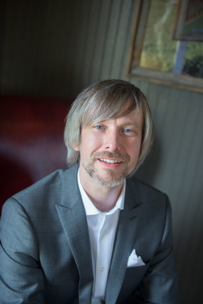 man with long brown hair, blue eyes, in a grey suit